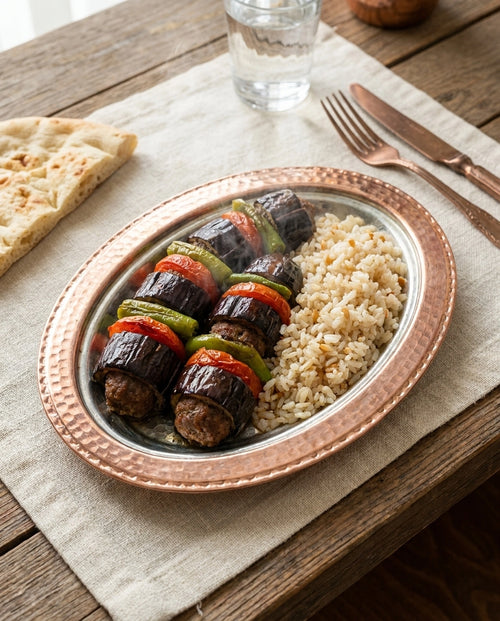 Ahşap masada bakır kayık tabak içinde servis edilmiş patlıcan kebabı ve pilav sunumu. - Gaziantep Bakırcılık
