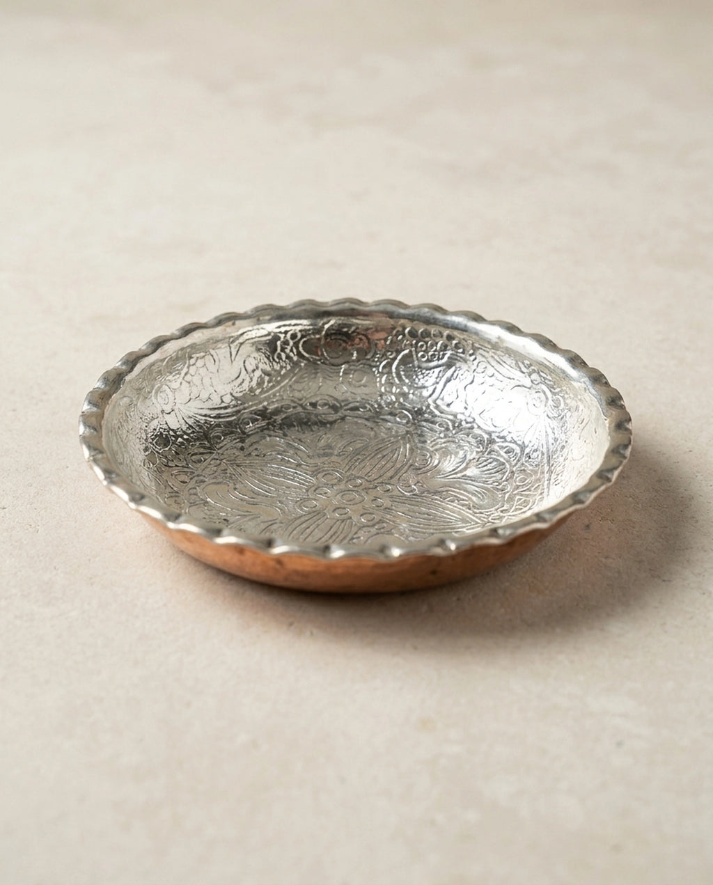 Taş zemin üzerinde duran içi çiçek motifleriyle işlenmiş dilimli kenarlı bakır sunumluk. - Gaziantep Bakırcılık
