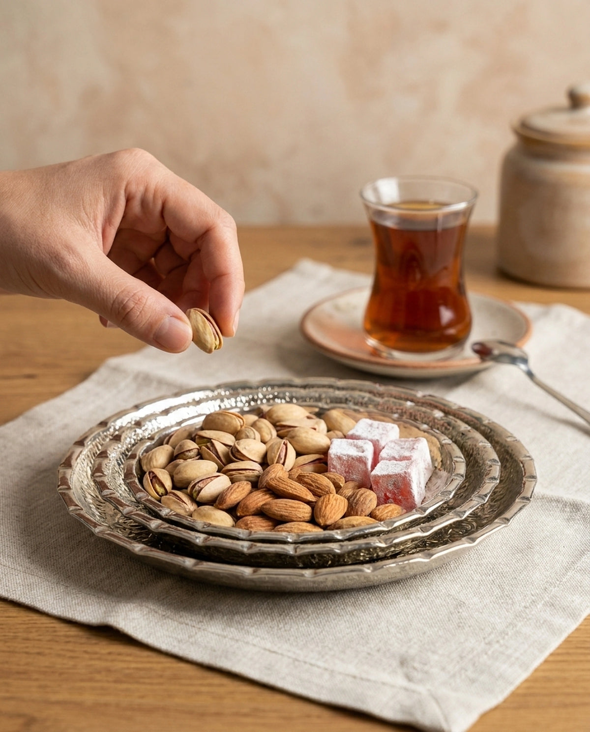 İşlemeli bakır çerezlik setinde kuruyemiş ve lokum sunumu yapılırken, bir elin kaseden fıstık aldığı çay saati konsepti. - Gaziantep Bakırcılık