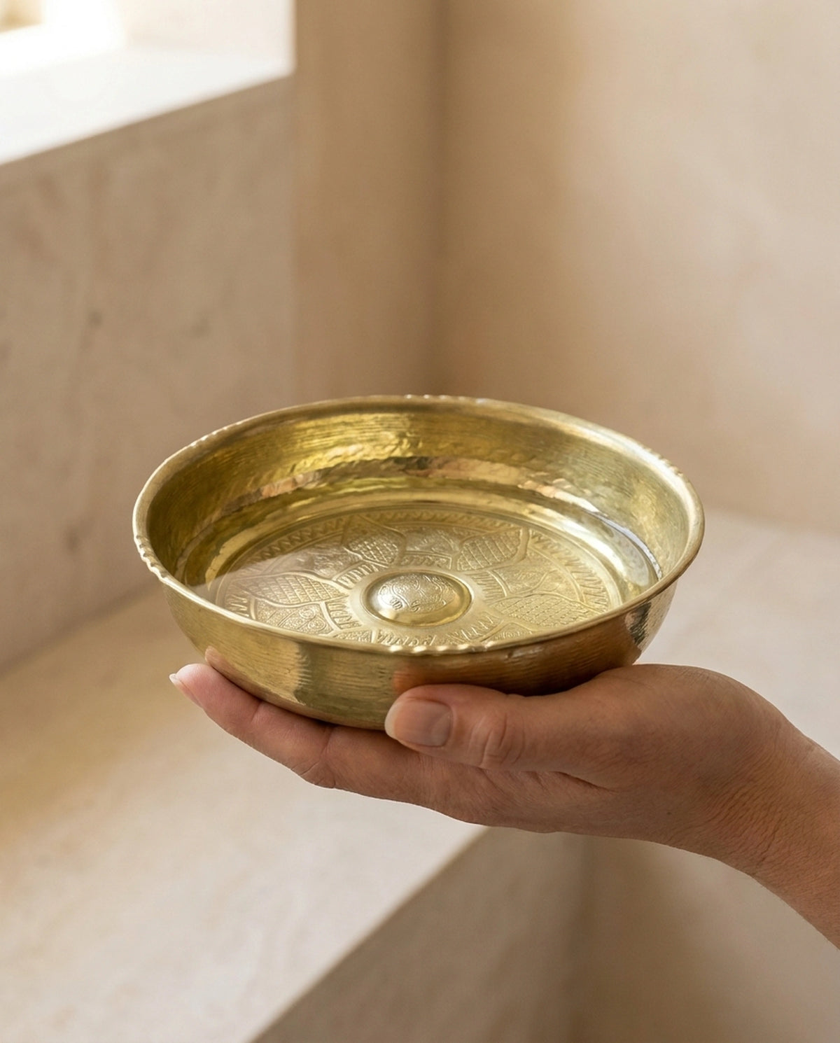 İki elin avuç içlerinde tuttuğu su dolu işlemeli sarı bakır hamam tasının yakından görünümü. - Gaziantep Bakırcılık