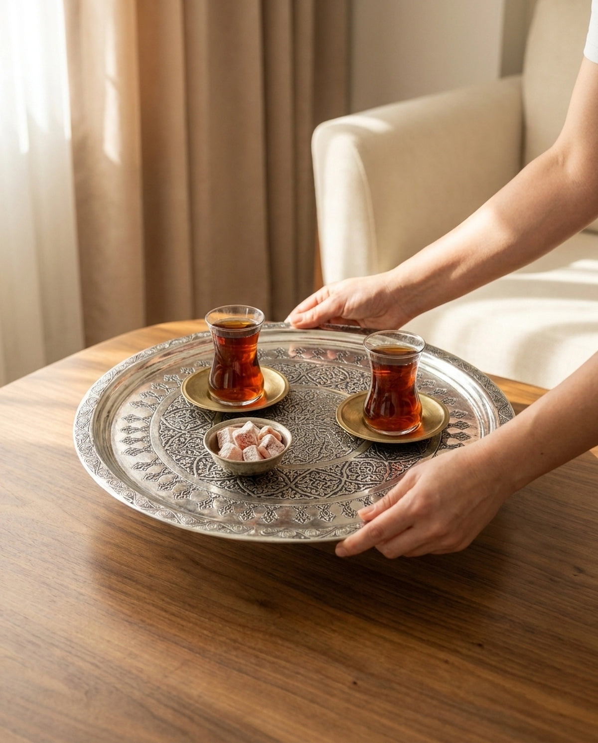 Ahşap masaya çay ve lokum servisi yapan ellerin tuttuğu gümüş işlemeli bakır tepsi - Gaziantep Bakırcılık