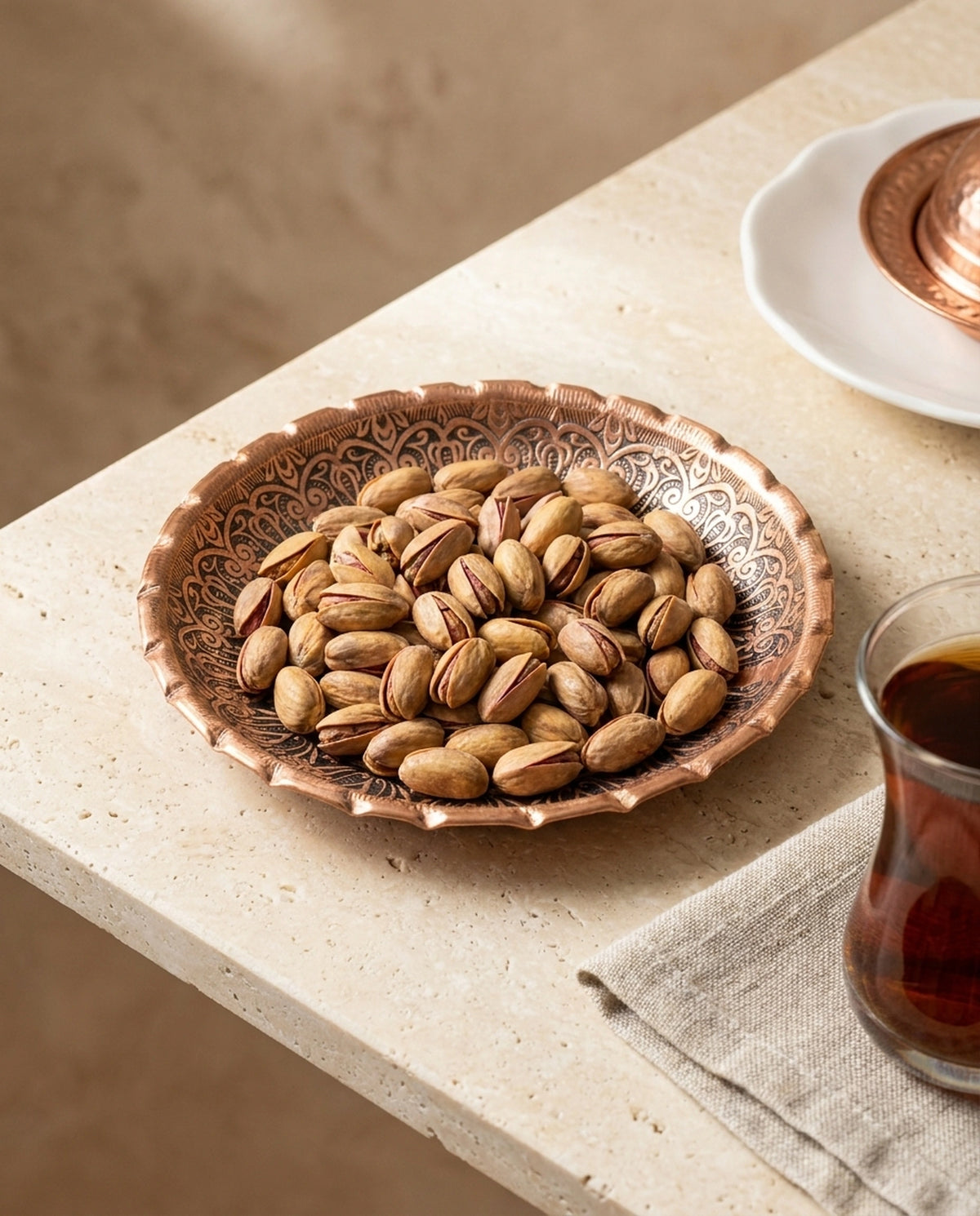 İçinde Antep fıstığı olan bakır çerezlik ve çay bardağı ile masa sunumu. - Gaziantep Bakırcılık