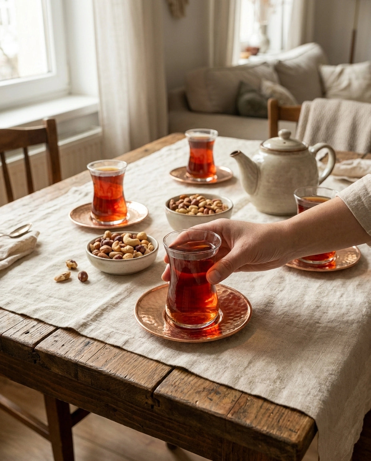Çay, kuruyemiş ve demlik bulunan masada bakır altlıklı çay bardağını tutan bir el. - Gaziantep Bakırcılık