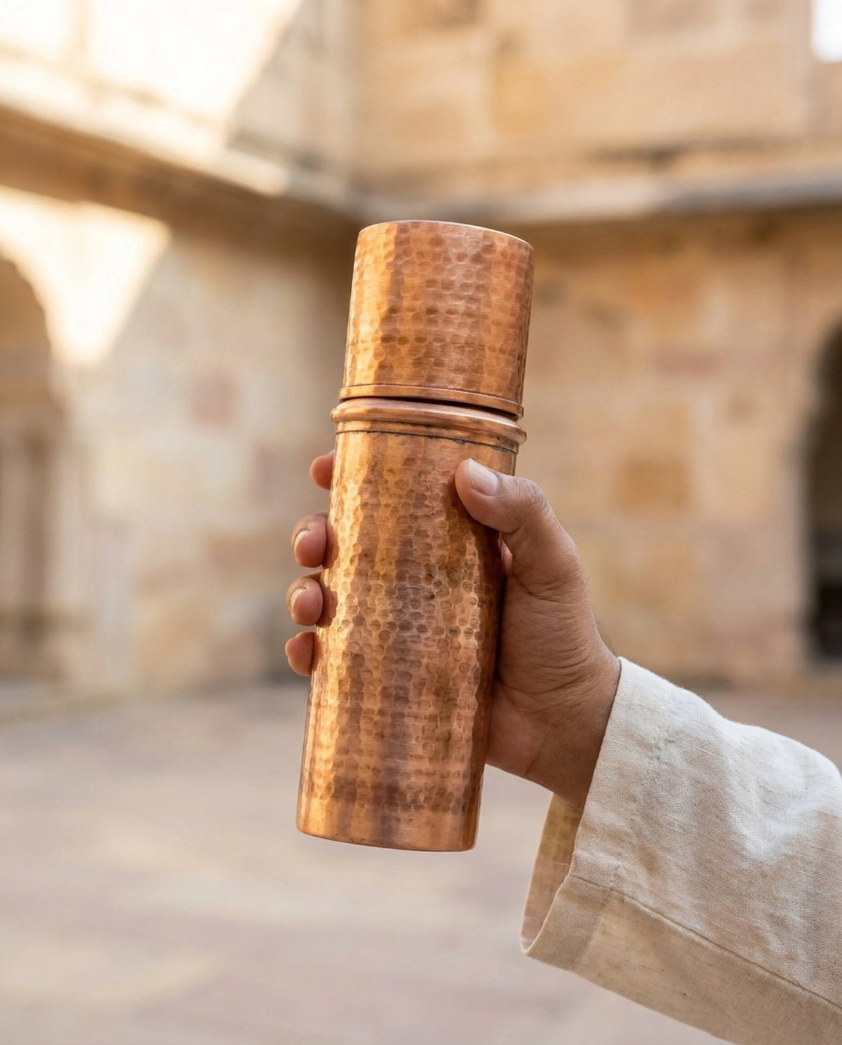 Tarihi taş yapı arka planında bir kişinin elinde tuttuğu dövme kızıl bakır matara. - Gaziantep Bakırcılık