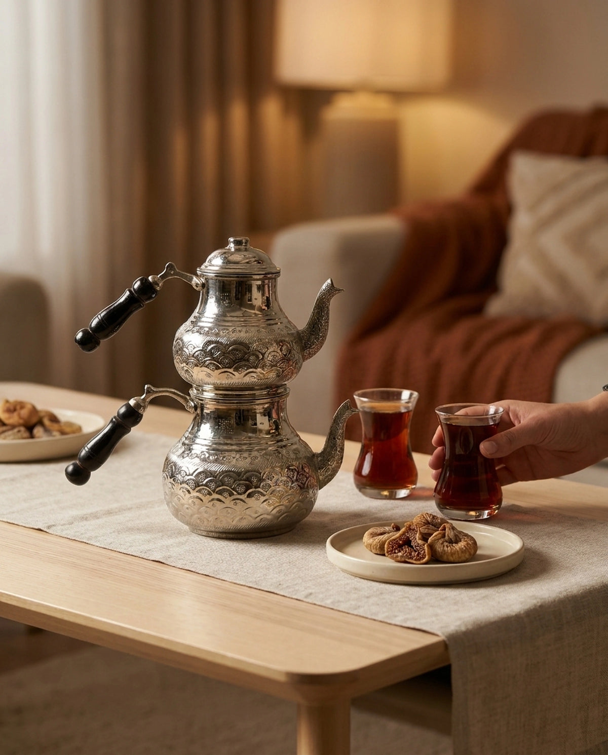 Loş bir salonda sehpa üzerinde bakır çaydanlık ve elde tutulan dolu çay bardağı. - Gaziantep Bakırcılık