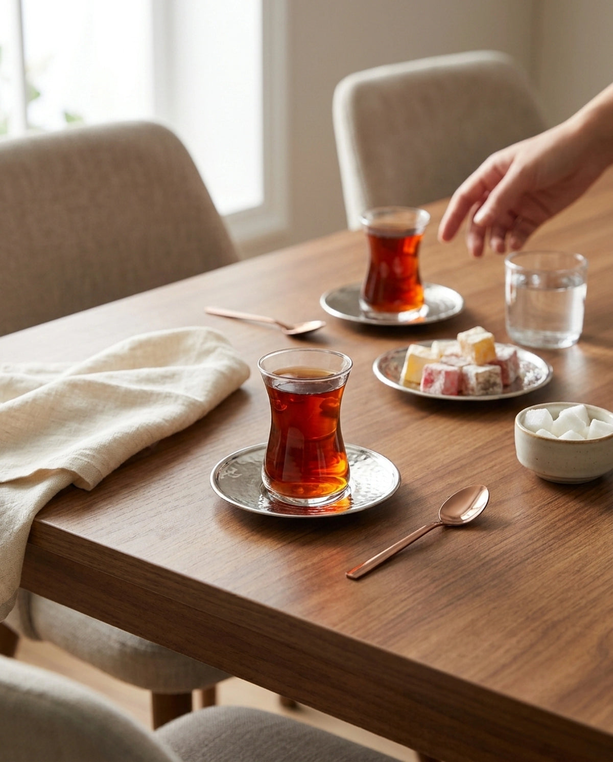 Ahşap masa üzerinde çay servis düzeni, iki adet bakır çay altlığı, dolu bardaklar ve lokum. - Gaziantep Bakırcılık