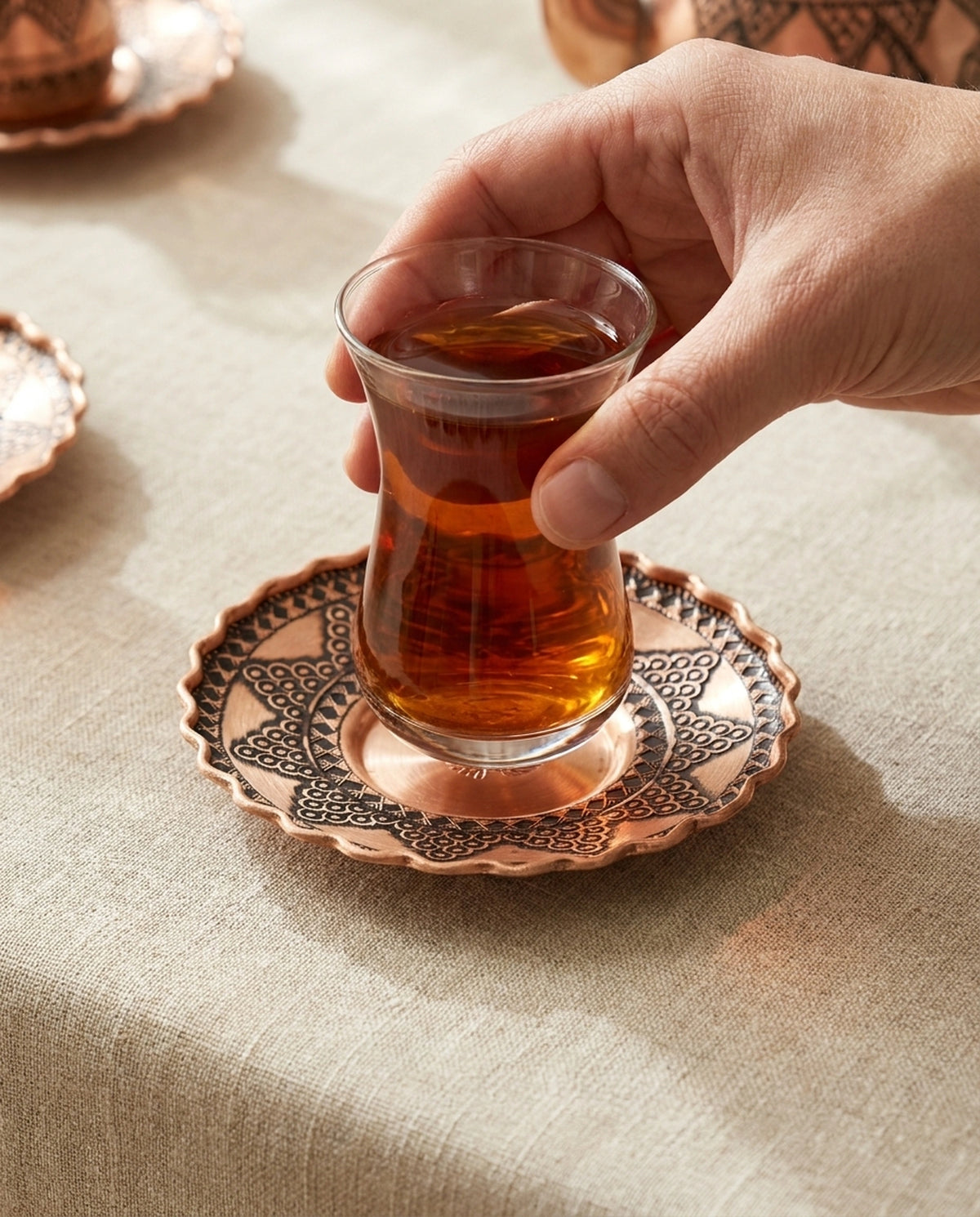 Bakır bardak altlığı üzerindeki çay dolu bardağı tutan bir elin yakından görünümü - Gaziantep Bakırcılık