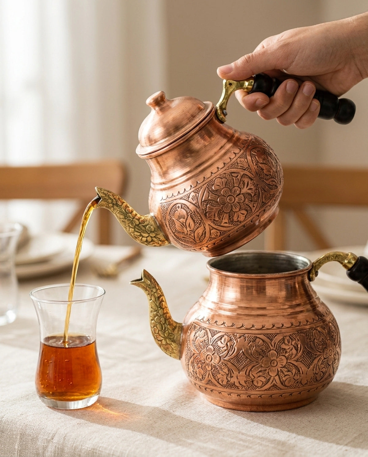 Bir elin üst bakır demlikten ince belli bardağa çay doldurduğu kullanım anı, alt suluk masada. - Gaziantep Bakırcılık
