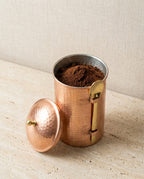 Kapağı açık, içi taze çekilmiş kahve dolu dövme bakır kabın ve yanındaki pirinç kaşığın görünümü. - Gaziantep Bakırcılık