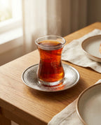 Ahşap masada işlemeli bakır altlık üzerinde sunulan dumanı tüten ince belli çay bardağı. - Gaziantep Bakırcılık