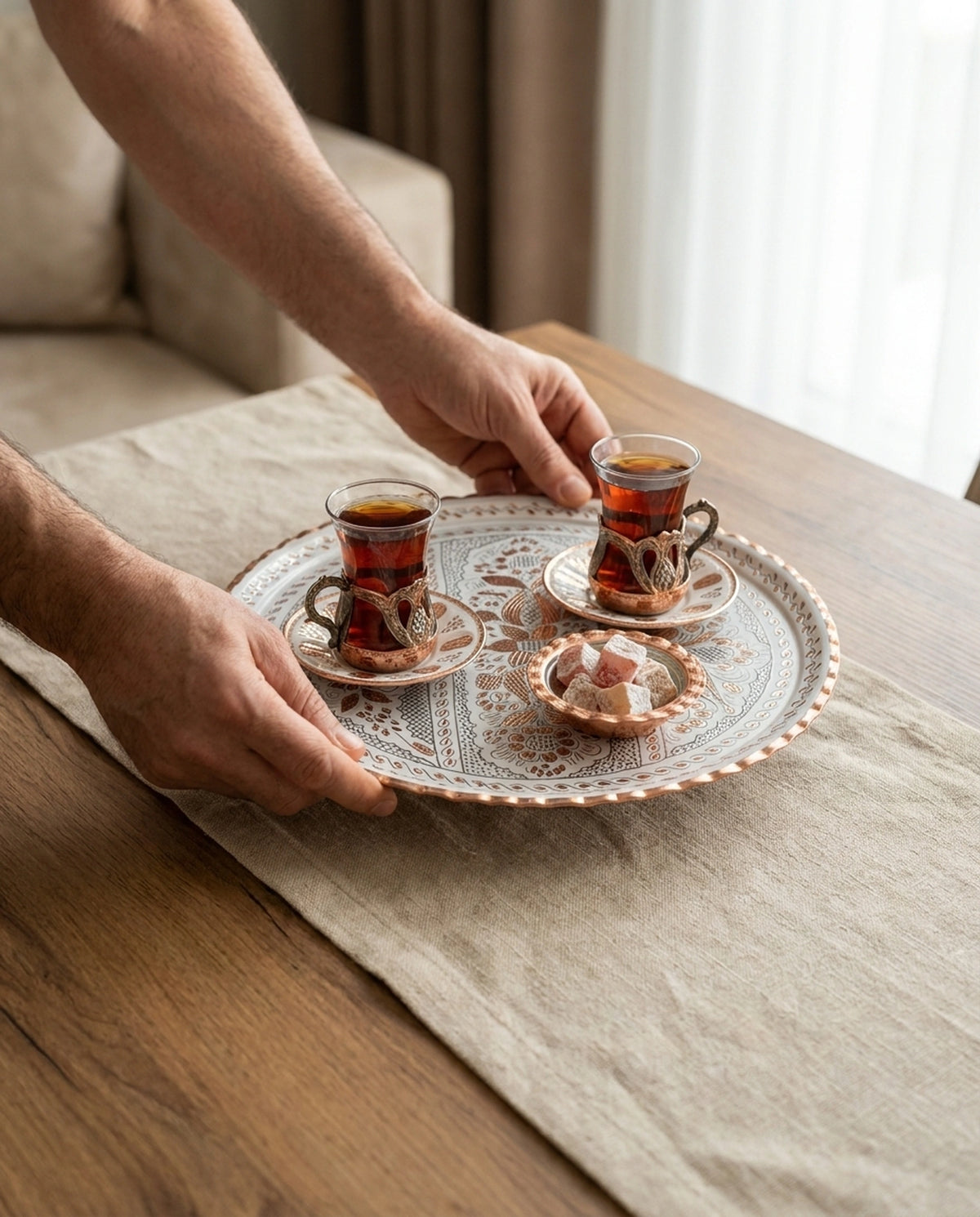 Ahşap masa üzerindeki örtüye çay ve lokum ikramlarıyla dolu beyaz bakır tepsiyi bırakan erkek elleri - Gaziantep Bakırcılık
