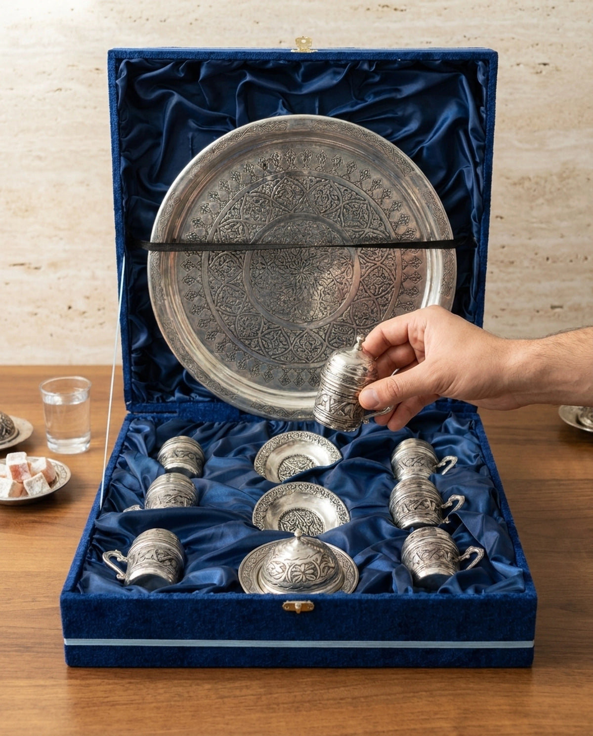 Kutudan kapaklı bakır fincanı çıkaran bir elin ve arka planda lokumun yer aldığı sunum detayı. - Gaziantep Bakırcılık