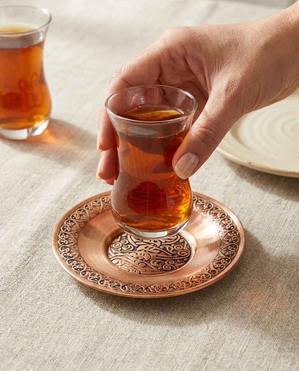 Bir kişinin ince belli çay bardağını motifli kızıl bakır çay bardak altlığının üzerine koyduğu an. - Gaziantep Bakırcılık