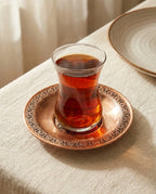 Rumi işlemeli kızıl bakır çay bardak altlığı üzerinde, dumanı tüten ince belli bardakta çay sunumu. - Gaziantep Bakırcılık
